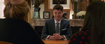 Movie still from “Ocean's Eight” (2018), directed by Gary Ross – A man sitting at a table in front of a statue; Medium shot, Over the shoulder angle