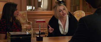 Movie still from “Ocean's Eight” (2018), directed by Gary Ross – A woman sitting in front of a wooden table; Medium shot, Over the shoulder angle