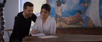 Movie still from “Ocean's Eight” (2018), directed by Gary Ross – A man and a woman sitting at a table writing on a piece of paper; Medium shot, Over the shoulder angle