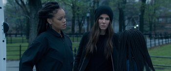 Movie still from “Ocean's Eight” (2018), directed by Gary Ross – Two young women standing next to each other in a park; Close Up shot, Over the shoulder angle