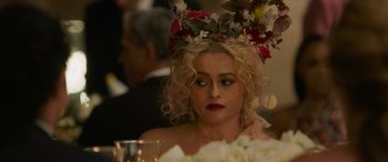 Movie still from “Ocean's Eight” (2018), directed by Gary Ross – A woman wearing a floral headpiece sitting at a dinner table; Close Up shot, Over the shoulder angle