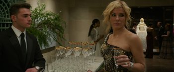 Movie still from “Ocean's Eight” (2018), directed by Gary Ross – A woman standing next to a table full of wine glasses; Medium shot, Over the shoulder angle