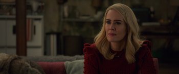 Movie still from “Ocean's Eight” (2018), directed by Gary Ross – A woman sitting on top of a couch wearing a red sweater; Close Up shot, Over the shoulder angle