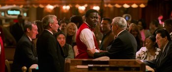 Movie still from “Ocean's Eleven” (2001), directed by Steven Soderbergh – A group of people gathered around a man in a red vest; Medium shot, Over the shoulder angle