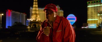 Movie still from “Ocean's Eleven” (2001), directed by Steven Soderbergh – An older man in a red shirt and a red hat is holding a cigarette; Close Up shot, Low angle