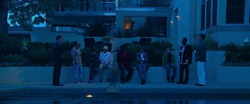 Movie still from “Ocean's Thirteen” (2007), directed by Steven Soderbergh – A group of people sitting on a wall by a pool at night; Wide shot, High angle