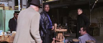 Movie still from “Ocean's Twelve” (2004), directed by Steven Soderbergh – A man standing next to another man in front of a wooden table; Medium shot, Over the shoulder angle
