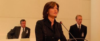 Movie still from “Ocean's Twelve” (2004), directed by Steven Soderbergh – A woman is speaking at a podium in front of a microphone; Medium shot, Low angle