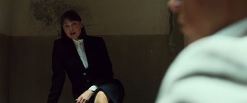 Movie still from “Ocean's Twelve” (2004), directed by Steven Soderbergh – A woman in a suit sitting on a chair in front of a wall; Medium shot, Over the shoulder angle
