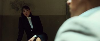 Movie still from “Ocean's Twelve” (2004), directed by Steven Soderbergh – A woman in a suit sitting on a chair; Medium shot, Over the shoulder angle