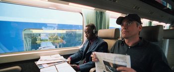 Movie still from “Ocean's Twelve” (2004), directed by Steven Soderbergh – Two men are sitting on a train while listening to music; Medium shot, Over the shoulder angle