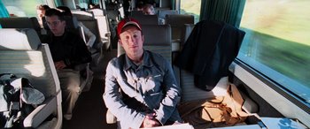 Movie still from “Ocean's Twelve” (2004), directed by Steven Soderbergh – A man sitting on a bus with a red hat; Medium shot, High angle