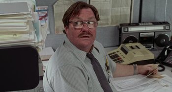 Movie still from “Office Space” (1999), directed by Mike Judge – A man with a beard and glasses is sitting in an office; Close Up shot, Low angle