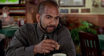 Movie still from “Office Space” (1999), directed by Mike Judge – A person sitting at a table with a cup; Close Up shot, Over the shoulder angle