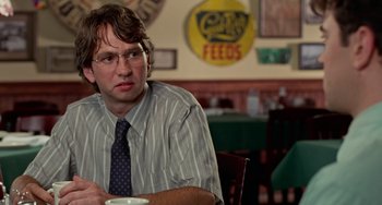 Movie still from “Office Space” (1999), directed by Mike Judge – A man sitting at a table in front of a cup; Close Up shot, Over the shoulder angle