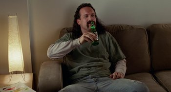 Movie still from “Office Space” (1999), directed by Mike Judge – A man sitting on a couch drinking a bottle of beer; Medium shot, High angle