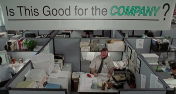 Movie still from “Office Space” (1999), directed by Mike Judge – A man sitting at a desk in an office; Wide shot, Low angle