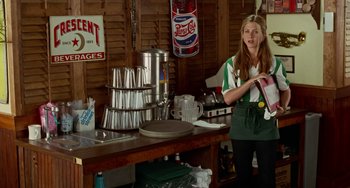 Movie still from “Office Space” (1999), directed by Mike Judge – A woman standing in front of a table with cups on top of it; Medium shot, Over the shoulder angle