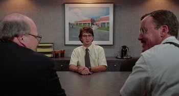 Movie still from “Office Space” (1999), directed by Mike Judge – A man sitting at a table in front of a painting; Medium shot, Over the shoulder angle