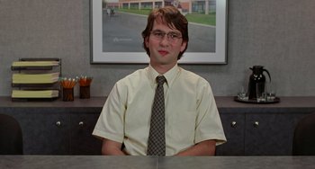 Movie still from “Office Space” (1999), directed by Mike Judge – A man sitting at a desk in front of a picture; Medium shot, Low angle
