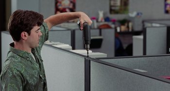 Movie still from “Office Space” (1999), directed by Mike Judge – A woman using a drill on a cubicle wall in an office setting; Medium shot, Low angle