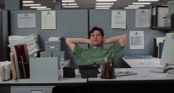 Movie still from “Office Space” (1999), directed by Mike Judge – A man sitting at a desk with his hands behind his head; Medium shot, Low angle