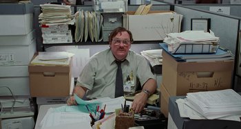 Movie still from “Office Space” (1999), directed by Mike Judge – A man sitting at a desk in an office; Medium shot, High angle