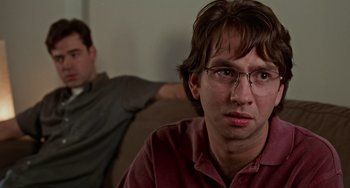Movie still from “Office Space” (1999), directed by Mike Judge – A man sitting on a couch next to another man; Close Up shot, Over the shoulder angle