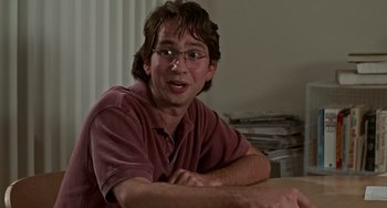 Movie still from “Office Space” (1999), directed by Mike Judge – A man sitting at a table with his arms crossed; Close Up shot, Low angle