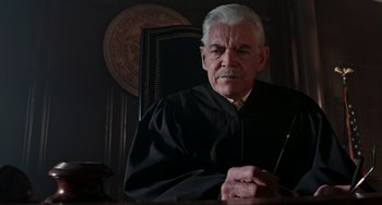 Movie still from “Office Space” (1999), directed by Mike Judge – An older man in a black robe sitting in a chair; Close Up shot, Low angle