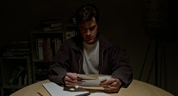 Movie still from “Office Space” (1999), directed by Mike Judge – A man sitting at a table looking at an open book; Medium shot, Low angle