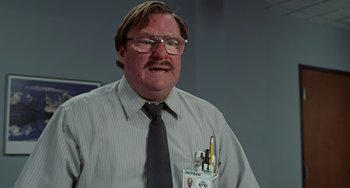 Movie still from “Office Space” (1999), directed by Mike Judge – A man wearing a shirt and tie with a box of pencils in front of him; Close Up shot, Low angle