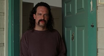 Movie still from “Office Space” (1999), directed by Mike Judge – A man with long black hair and a mustache; Close Up shot, Low angle