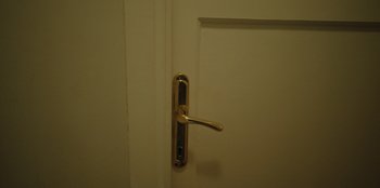 Movie still from “Oh Belinda” (2023), directed by Deniz Yorulmazer – A door handle on a white door; Extreme Close Up shot, High angle