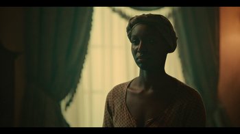 Movie still from “Atlanta” (2016), created by Donald Glover – A woman with a head wrap is standing by a window; Close Up shot, Over the shoulder angle
