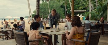 Movie still from “Old” (2021), directed by M. Night Shyamalan – A group of people sitting at a table with drinks; Medium shot, Over the shoulder angle