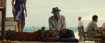 Movie still from “Old” (2021), directed by M. Night Shyamalan – An older man and a younger woman sitting next to each other on the beach; Medium shot, High angle