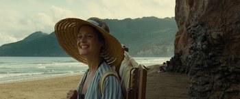 Movie still from “Old” (2021), directed by M. Night Shyamalan – A woman in a straw hat is standing on the beach; Medium shot, High angle