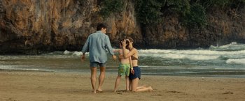 Movie still from “Old” (2021), directed by M. Night Shyamalan – A woman kneeling on the beach next to a man and a boy; Wide shot, High angle