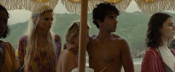 Movie still from “Old” (2021), directed by M. Night Shyamalan – A group of people standing under an umbrella on the beach; Medium shot, Over the shoulder angle