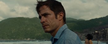 Movie still from “Old” (2021), directed by M. Night Shyamalan – A person wearing a blue shirt near a body of water; Close Up shot, Over the shoulder angle