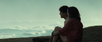 Movie still from “Old” (2021), directed by M. Night Shyamalan – A man and a woman sitting next to each other on top of a hill; Medium shot, Over the shoulder angle