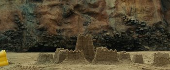 Movie still from “Old” (2021), directed by M. Night Shyamalan – A sand castle in front of a rock wall; Extreme Wide shot, Low angle