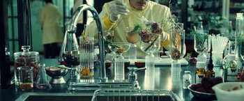 Movie still from “Old” (2021), directed by M. Night Shyamalan – A person in a yellow shirt is working in a lab; Medium shot, Over the shoulder angle
