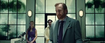 Movie still from “Old” (2021), directed by M. Night Shyamalan – A man in a suit and tie standing next to two other people; Medium shot, Over the shoulder angle