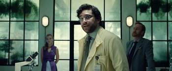 Movie still from “Old” (2021), directed by M. Night Shyamalan – A man in a suit and tie standing next to a woman in a purple dress; Medium shot, Low angle