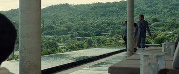 Movie still from “Old” (2021), directed by M. Night Shyamalan – Two people standing next to a pool overlooking a lush green hillside; Extreme Wide shot, Over the shoulder angle
