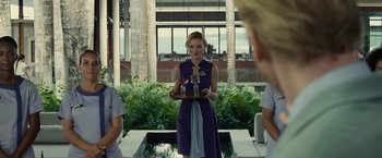 Movie still from “Old” (2021), directed by M. Night Shyamalan – A woman in a purple dress holding a trophy in front of a group of people; Medium shot, Over the shoulder angle