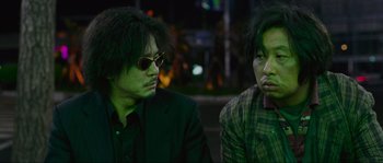 Movie still from “Oldboy” (2003), directed by Park Chan-wook – A couple of men sitting next to each other on a street; Close Up shot, Low angle