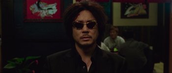 Movie still from “Oldboy” (2003), directed by Park Chan-wook – A man wearing sunglasses and a black shirt; Close Up shot, Low angle